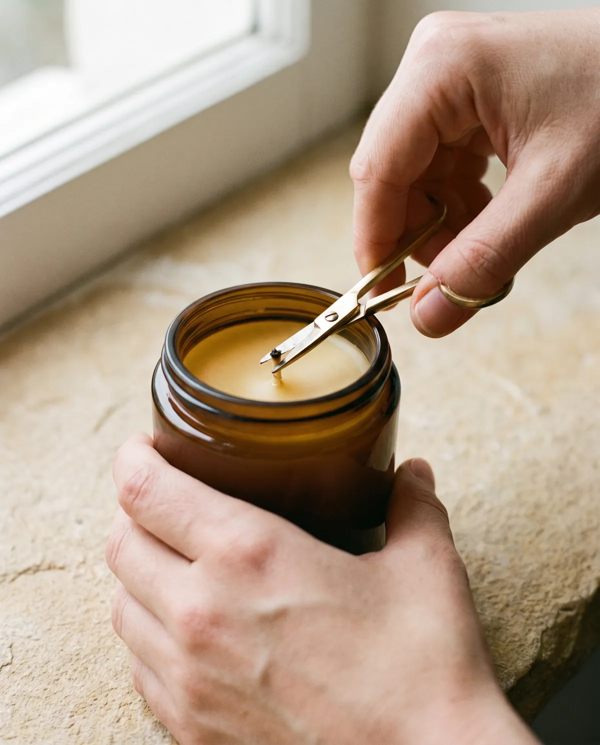 Hands trimming the wick of a candle with a brass wick trimmer